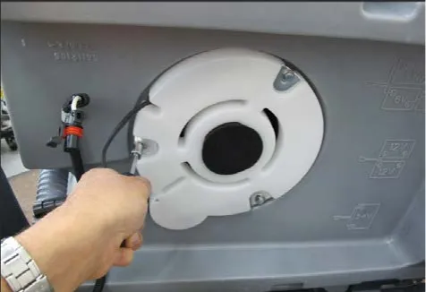 A hand using a screwdriver to remove a mounting screw from the white vacuum motor cover