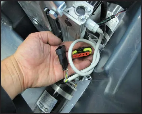Photo of a hand holding the disconnected actuator electrical connector next to the actuator.