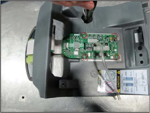 Cover turned over on a bench with the four circuit board screws circled and a screwdriver on one