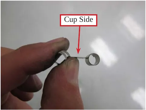 Photo of a brush spring held in fingers with an arrow and the label Cup Side.