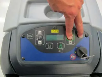 Hand on the membrane switch control panel with two fingers pressing the scrub on/off switch and the vacuum/wand switch, key switch at the lower right