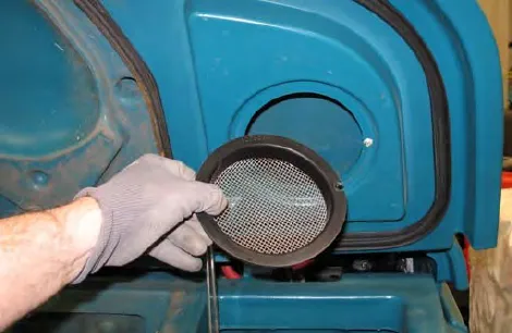A gloved hand holding the round vacuum screen removed from the recovery tank cover