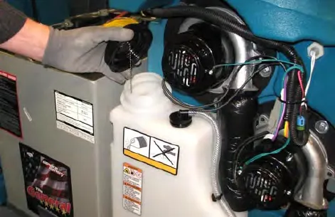 A gloved hand removing the cap from the white detergent tank behind the left shroud