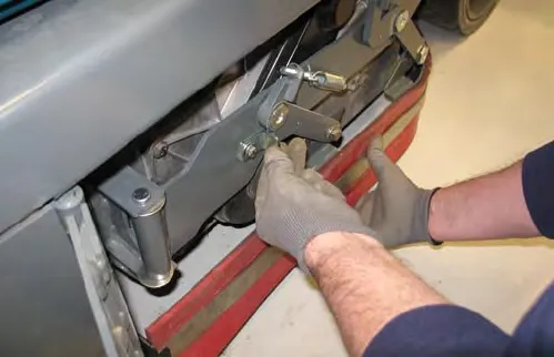 Two gloved hands lifting a side squeegee assembly and positioning the double scrub latch