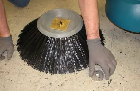 Hands holding the removed Pre-Sweep side brush and its retaining washer on the floor