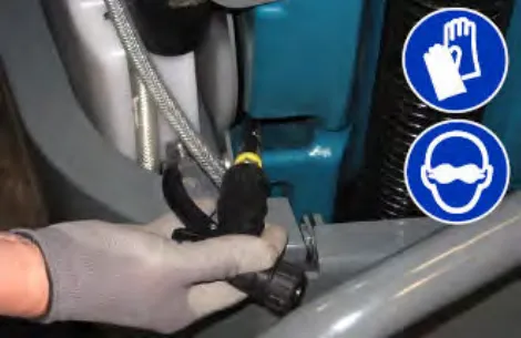 A gloved hand pulling the spray nozzle out from behind the left shroud, with glove and eye protection symbols