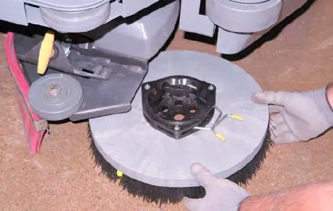Hands removing the side brush from under the side brush assembly