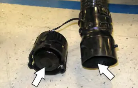 The drain nozzle plug and the drain hose cuff laid on the floor, with arrows pointing at the plug and the inside of the cuff