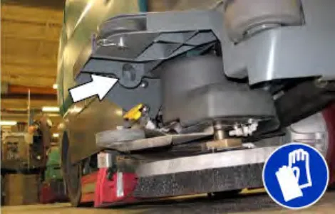 Step on top of the scrubbing side brush assembly with an arrow pointing to the tie-down point, plus glove symbol