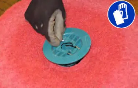 Hand squeezing the spring clip to remove the center disk from the pad driver, plus glove symbol