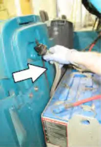 Hand unhooking the return line from the solution tank, with an arrow pointing to it
