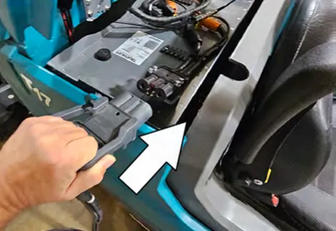 Hand plugging the charger connector into the battery charging port, with an arrow pointing to the port