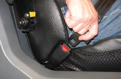 A hand pulling the seat belt across to the buckle on the deluxe seat