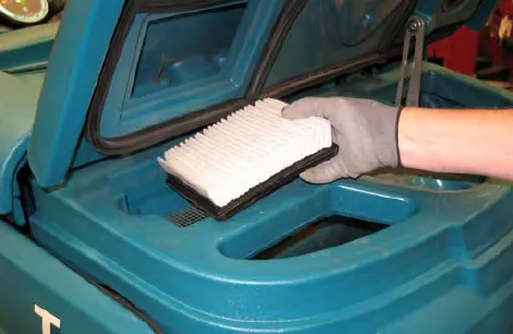 A gloved hand holding the white pleated vacuum fan inlet filter above its housing