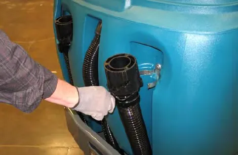 A hand inserting the drain hose into the clip on the side of the recovery tank