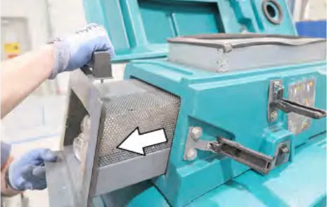 Hand lifting the debris tray out of the vacuum chamber, with an arrow showing the direction