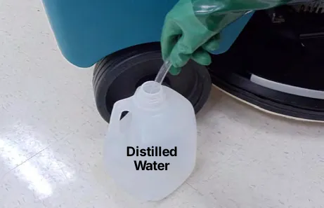 Hand pump hose placed in a jug labeled Distilled Water