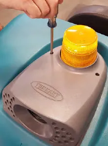 Screwdriver removing the cover of the amber backup alarm light