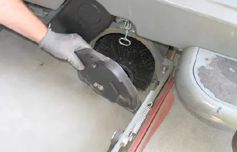 Gloved hand taking the idler plate off the end of the cylindrical brush