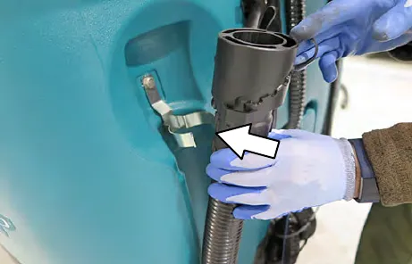 Drain hose being inserted into the clip on the solution tank, with an arrow to the clip