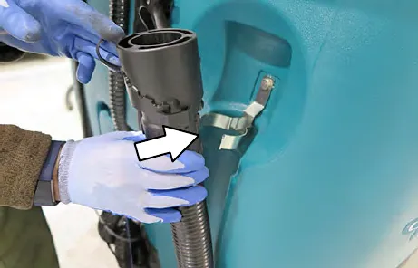 Drain hose being inserted into the clip on the recovery tank, with an arrow to the clip