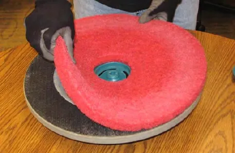 Gloved hands peeling the red scrub pad off the pad driver