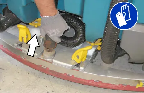 Gloved hand pulling the vacuum hose off the rear squeegee assembly, with an arrow showing the direction; gloves must be worn