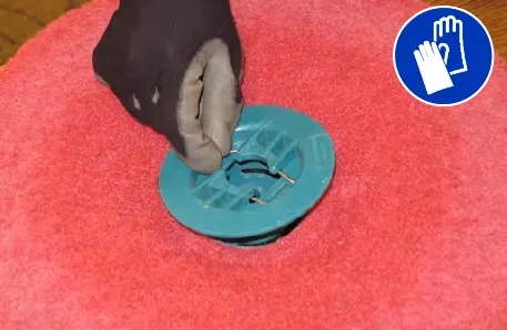 Gloved hand squeezing the spring clip on the center disk of a pad; gloves must be worn