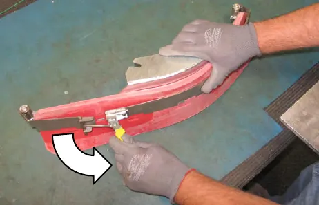 Gloved hand loosening the retaining band latch on the removed squeegee assembly, with an arrow showing the direction