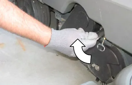 Gloved hand lifting the idler plate retainer handle, with an arrow showing the direction
