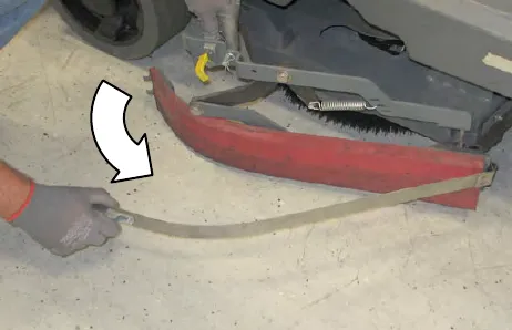 Gloved hand pulling the retaining band away from the squeegee blade, with an arrow showing the direction