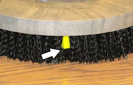 Edge of a disk brush with an arrow pointing to a yellow bristle wear indicator