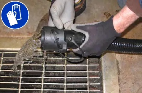 Gloved hands holding the open drain nozzle over a floor drain