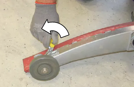 Gloved hand lifting the retainer latch, with an arrow showing the direction