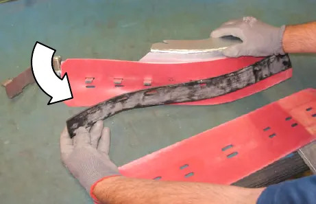 Hands pulling the retainer strip out from between the squeegee blades, with an arrow showing the direction
