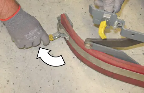 Gloved hand unhooking the retaining band latch, with an arrow showing the direction