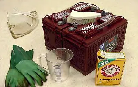Scrub brush, baking soda, measuring cup, gloves and eye protection used to clean a battery
