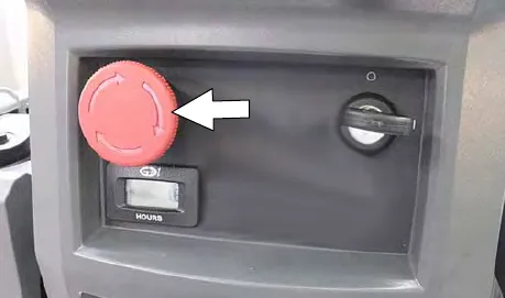 Red emergency shut-off button on the control panel, marked by an arrow